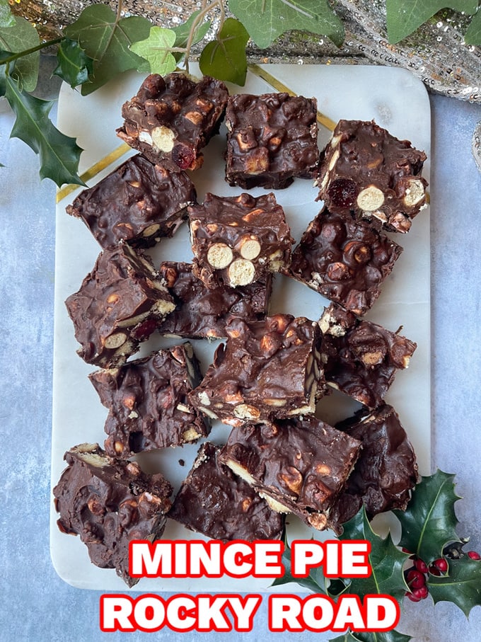 Mince Pie Rocky Road cut into squares and served on a white marble chopping board with fresh holly sprigs in the background.