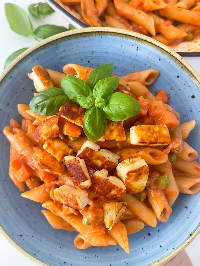 One pot smoky halloumi pasta, served in a blue pasta bowl with a garnish of basil leaves. 
