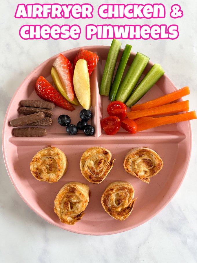 Airfryer chicken & cheese pinwheels served on a child's divided plate along with slices of fresh fruit and veggies.