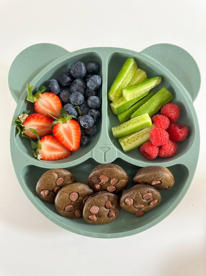 Mini chocolate spinach muffins served in a childs divided plate along with chopped veggies and berries.