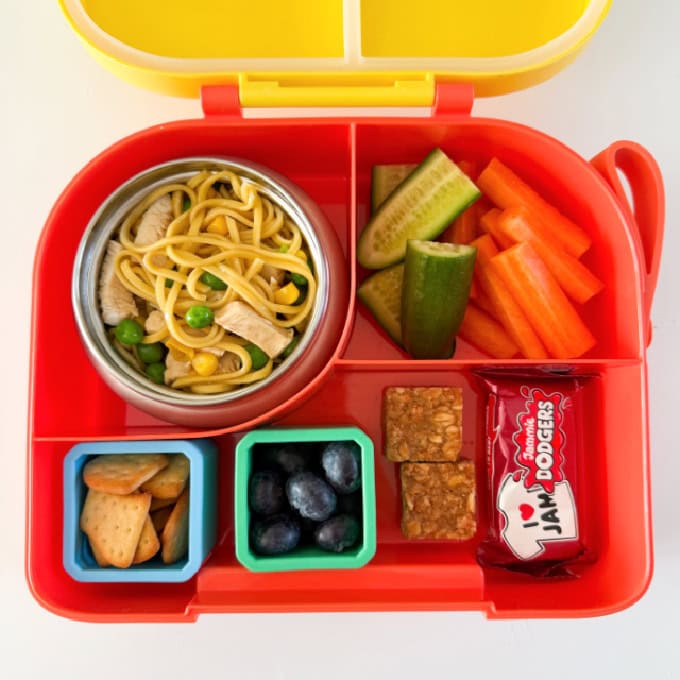 Chicken noodles served in a hot &  cold lunch box with sliced carrots and cucumber.